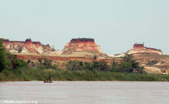 Boys in pirogue at a  distance with clay laterite banks in background (Manambolo)